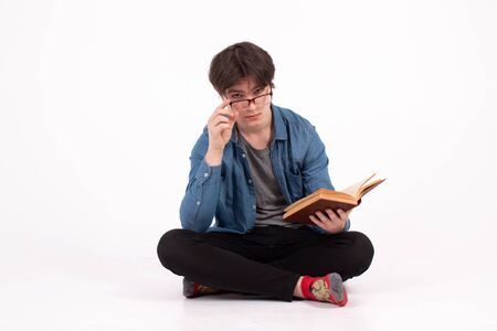 Portrait of young man in eyeglasses drinking coffee and looking at open book isolated on a white...