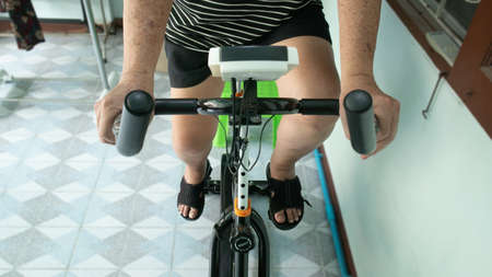 The oldman cardio himself at home by Exercise bike, Front view, casual wear with Workout shorts...