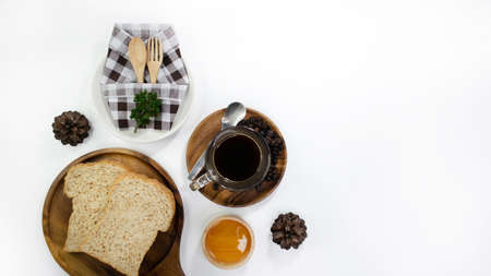 Breakfast top view on white background, copy space. spoon & fork in plaid napkin, bread, honey syrup and coffee for breakfast, decorate with mini christmas wreath, mini present and pine cones.の写真素材