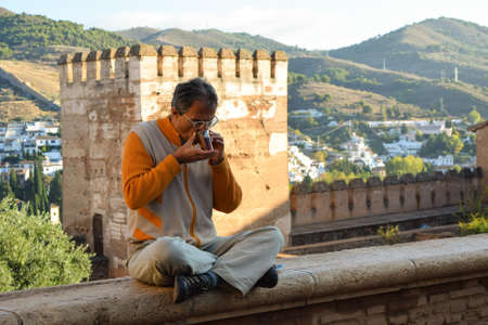 Inner peace, calmness and presence is illustrated by a man who enjoys the environment in the historical palace of Alhambra in Granada, with a cup of tea in his hands.のeditorial素材
