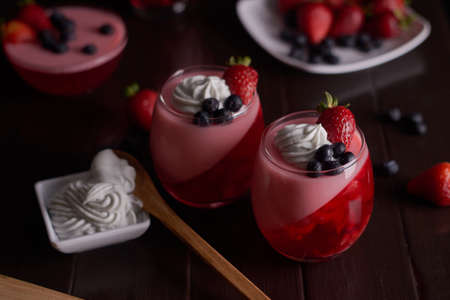 Red fruit jelly desserts with chantilly cream in glass cups with blueberries and strawberries and...