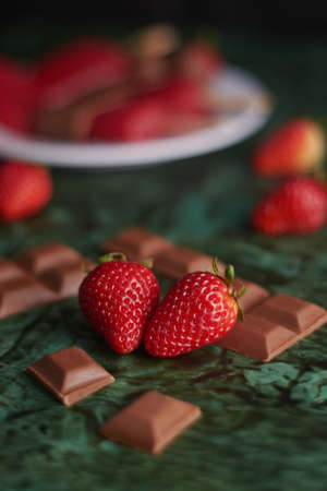 fresh strawberries with chocolate pieces around on green background with texturesの写真素材