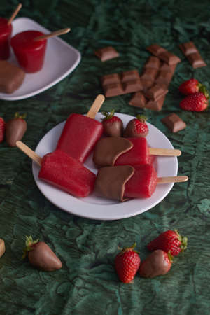 Strawberry and chocolate popsicles on white ceramic cup on dark green backgroundの写真素材