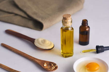olive oil mask in glass jar egg and mayonnaise on spoon and vitamin E with white backgroundの写真素材