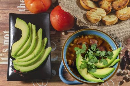 stew of chorizo ââand chickpeas, on a blue plate with avocado and toast garnished with cilantro on a table decorated in low key lightの写真素材