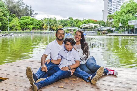 couple of Latin American men and women, with boy suffers autism, happy in a portrait family outdoors together in a park, the three laughing huggingの写真素材