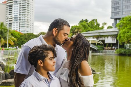 couple of Latin American men and women, with boy suffers autism, happy in a portrait family outdoors together in a park, the three laughing huggingの写真素材