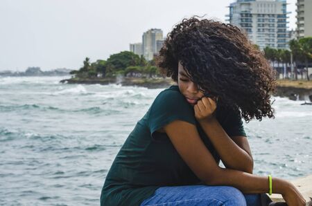 Young girl with black hair, laughing hair sitting on her back to the Caribbean Sea, enjoying a summer day with the wind in her hair, lifestyle portraitの写真素材