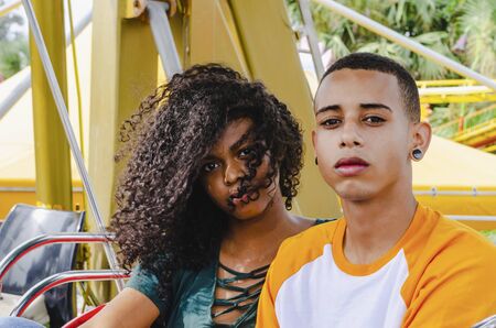 Young Latino couple sitting on a ferris wheel looking at cameraの写真素材