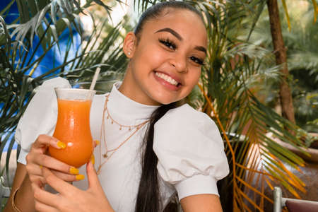 young woman spending time in outdoor restaurant having a cocktail and taking selfieの写真素材