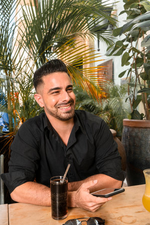 young man spending time in outdoor restaurant having a cocktail and taking selfieの写真素材