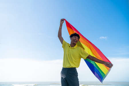 Young gay man proudly holding the lgbt flag in his hands in front of the seaの写真素材
