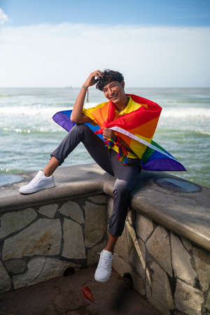 Young gay man proudly holding the lgbt flag in his hands in front of the seaの写真素材