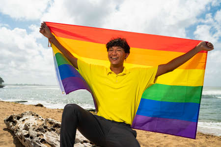 Young gay man proudly holding the lgbt flag in his handsの写真素材