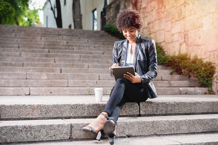 Latin businesswoman drinking coffee. Smiling businesswoman networking wiht tablet and cellphone outsideの写真素材