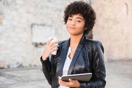Latin businesswoman drinking coffee. Smiling businesswoman networking wiht tablet and cellphone...