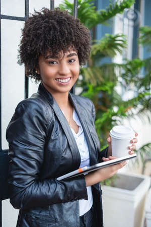 Latin businesswoman drinking coffee. Smiling businesswoman networking wiht tablet and cellphoneの写真素材