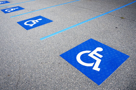 International handicapped symbol painted in bright blue on a shopping center parking space. The space is clearly marked on either side with additional white diagonal stripes.の写真素材