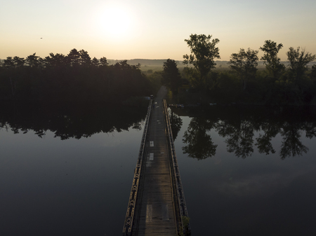 Old wooden bridge with rails over river against sunset background. Tisa River in Vojvodina region, Serbia.の写真素材