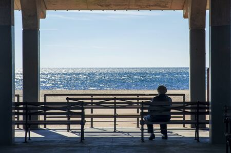 BROOKLYN, NEW YORK, USA - OCTOBER 27: Lonely senior woman sitting alone and looking the sea on Coney Island Board Walk in the sunny day at Brighton Beach, Brooklyn NY at October 27, 2013.のeditorial素材