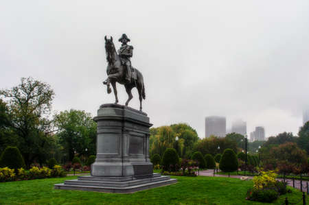 George Washington Monument in Boston Public Garden in fall foggy weather with a lot of high modern...