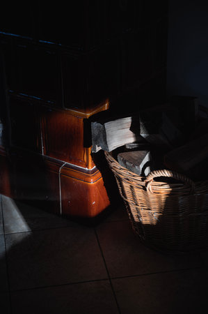 Woodpile in a wicker basket next to a traditional fire place lit by morning sunlight, cozy worm home winter atmosphereの写真素材
