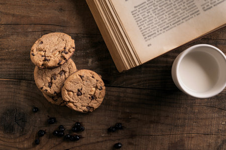 Home made Crispy Chocolate Cookies with Blueberries and Milk on Rustic Wooden table and Old Cook Book in the backgroundの写真素材