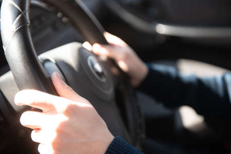 The man is sitting in the car and holding his hands behind the wheel