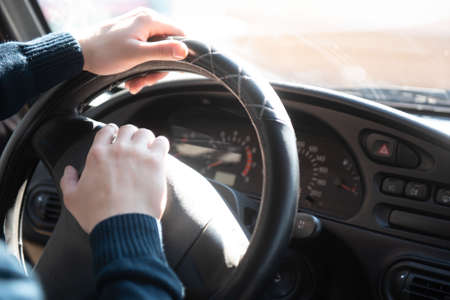 The man is sitting in the car and holding his hands behind the wheel