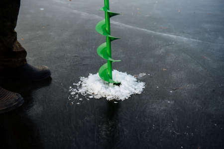 Fisherman drills a hole in the winter on the river. Winter fishing