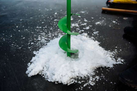 Fisherman drills a hole in the winter on the river. Winter fishingの写真素材