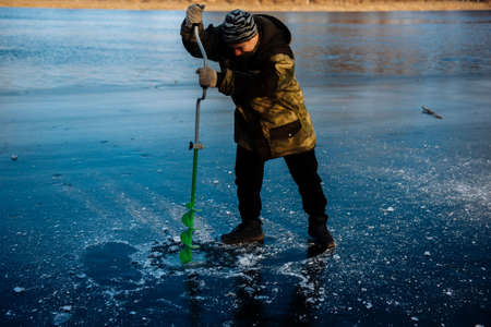 Fisherman drills a hole in the winter on the river. Winter fishingの写真素材