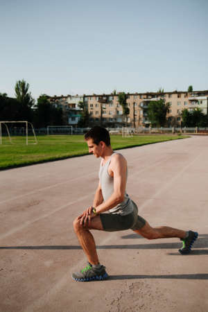 Athlete is warming up at the stadium. Male athlete is warming up at the stadium. Training at the stadium in the morning. Male runner warming up before training.の写真素材