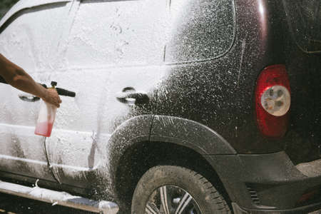 A man sprays a cleaning agent with a high pressure washer on a car. The car washes with a means of...