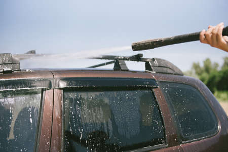 A man washes a car with a high pressure washer. A man washes a car. A car washer with high pressure...