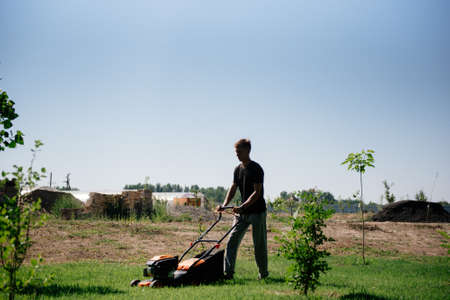 The gardener mows the lawn in the garden with a lawn mower in summer close up