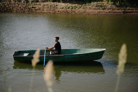 A young man swims in a small wooden boat with oars on the riverの写真素材