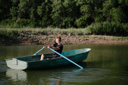A young man swims in a small wooden boat with oars on the river