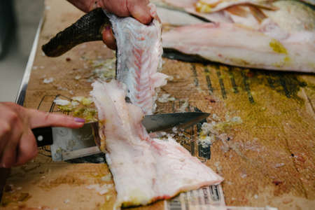 The cook cuts a large fish with a knife on the table in the kitchen close-up