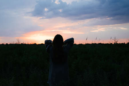 Cheerful young woman in white dress walking through beautiful lavender filed at golden sunset in summerの写真素材