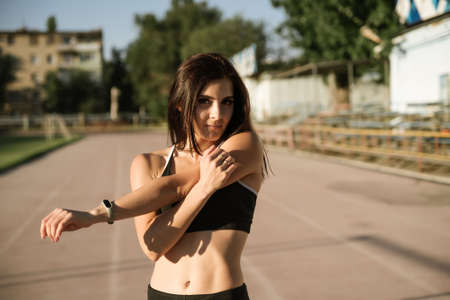 Shot of flexible young woman warms up before jogging on stadium, wears sportsclothes, shows her...