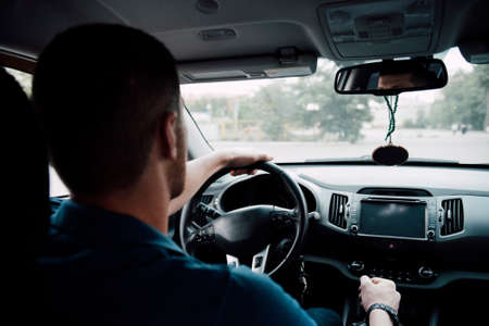 The driver man rides in the car behind the wheel view from the back seat. The driver behind the...