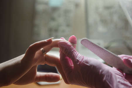 The manicurist handles nails with a nail file. Grinding the nail plate with a buffの写真素材