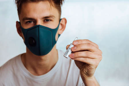 a man in a medical protective mask holds a test tube with the inscription covid-19