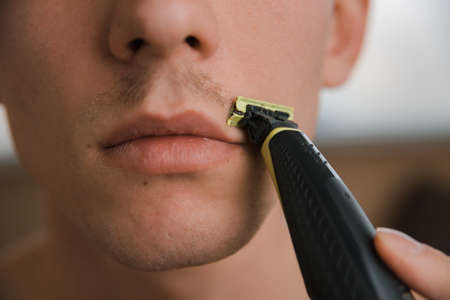 young man shaves off his mustache with a trimmer,close-up