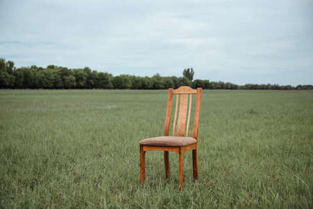 A wooden chair stands in the middle of a field.A chair in the middle of the field. The concept of...
