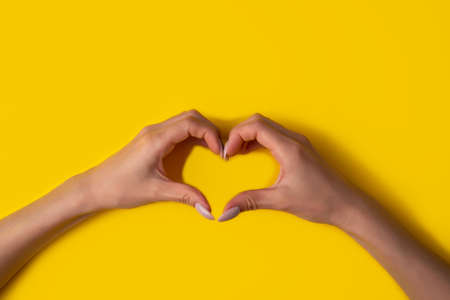 heart making woman's hands with manicure on yellow background, top view.The concept of love for your work and a beautiful manicure. Flat layの写真素材
