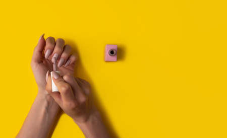 Close-up of a woman paints her nails with pink lacquer on a yellow background,top view. Manicure...