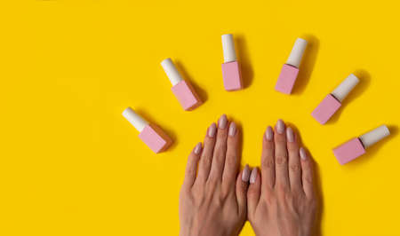 Gel polish of pink color and hands with manicure on a yellow background, top view. Woman hands and pink bottle of varnish on a yellow background. Manicure concept,bannerの写真素材