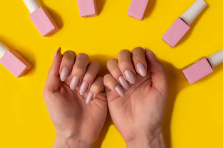 Gel polish of pink color and hands with manicure on a yellow background, top view. Woman hands and...